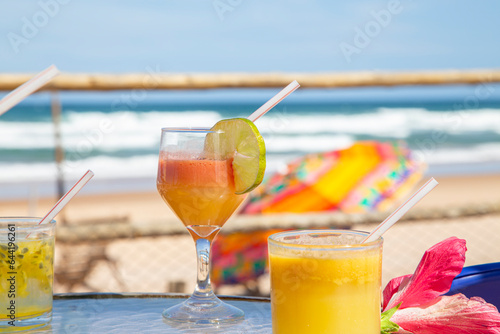 Drinks tropicais em mesa de praia no nordeste do Brasil. No fundo ondas do mar e um guarda sol colorido photo