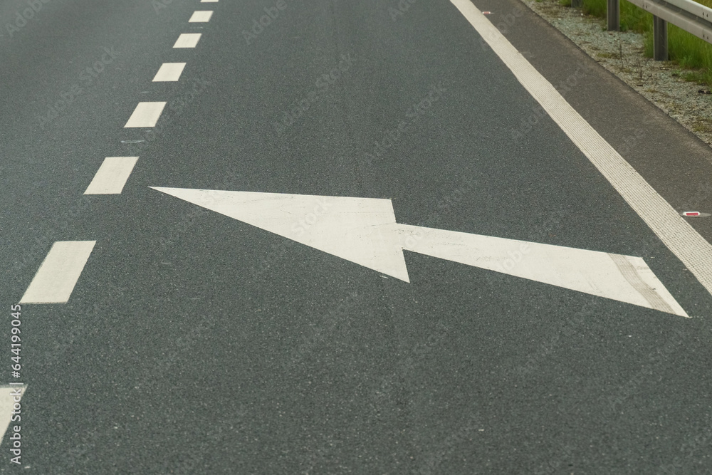 The white arrow on the pavement points to the left, the road narrows the carriageway The white arrow on the pavement points to the left, the road narrows the carriageway