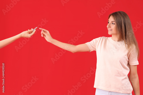 Young woman taking key from house on red background