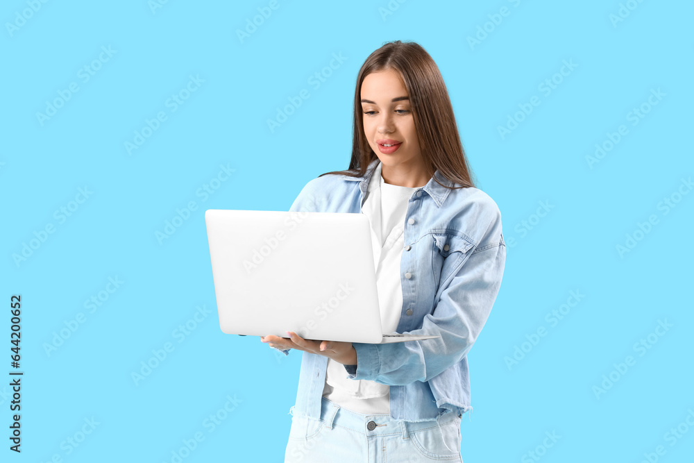 Young woman using laptop on blue background Young woman using laptop on blue background