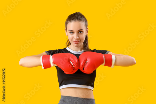 Sporty young woman with boxing gloves on yellow background © Pixel-Shot