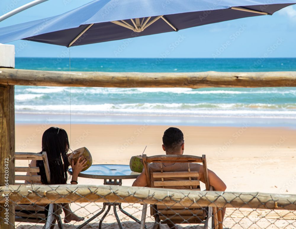 Jovem casal tomando água de coco na sombra em um resort em uma praia do nordeste brasileiro