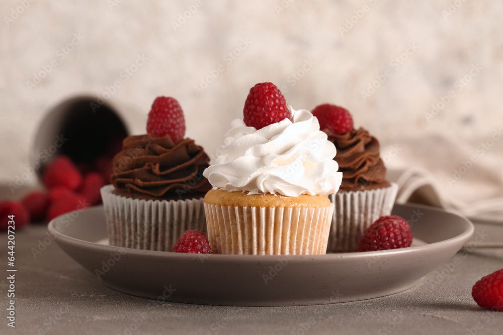 Plate of tasty cupcakes with raspberries on table