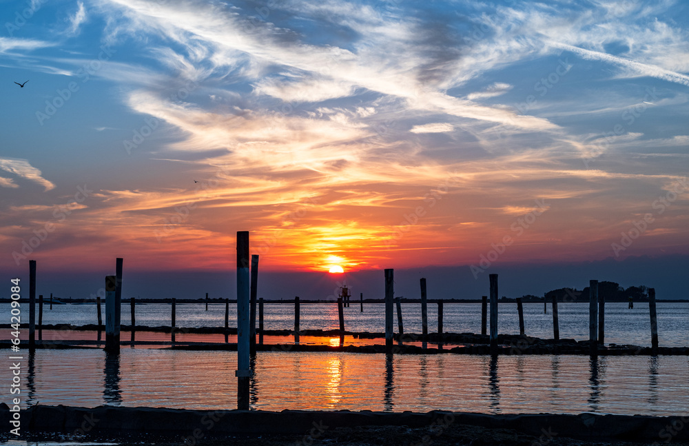 Sunset on the Grado Lagoon during a summer day. The sun is about to disappear over the horizon. Orange color and warm tones. A beautiful reflection on the sea. Taken near the Port.