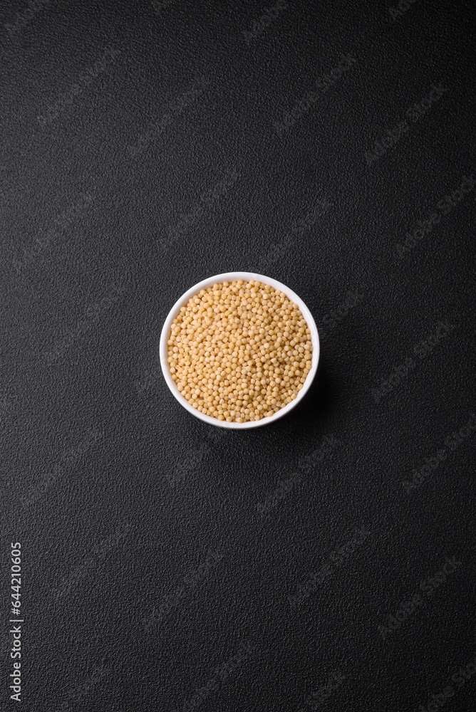 Raw ptitim pasta in a ceramic bowl on a dark concrete background