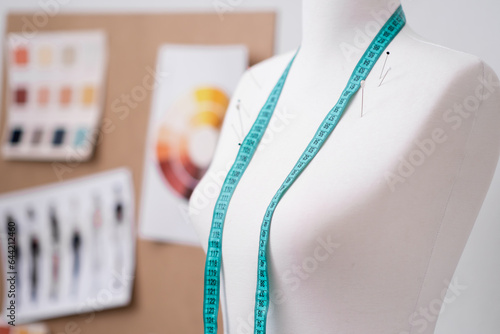 Green tape measure and pins on mannequin against board with swatches and sketches in fashion shop clothes sewing tools in contemporary atelier tailor studio closeup