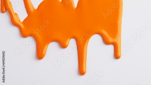 Liquid drops of orange paint color flowing on the white surface. Macro shot of orange paint dripping on the white canvas with copy space. Abstract art.