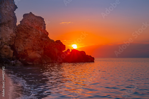 Beautiful sunset on the sea coast. Rocky coast of the sea, the leaving bright sun behind the mountain