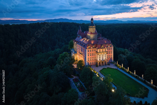 Evening aerial view of the illuminated Ksiaz Castle, Schloss Fürstenstein, a beautiful castle standing on a rock surrounded by forest in Lower Silesia Voivodeship, Poland. 