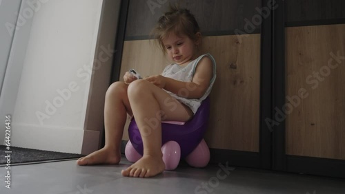 Toddler baby girl going to the toilet sitting on the potty, indoors in the living room. Baby learning to go to the toilet on lifestyle potty.