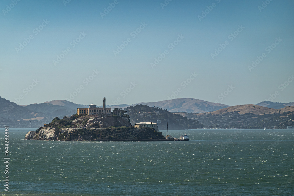 San Francisco, CA, USA - July 13, 2023: South tip of Alcatraz island where ferry leaves under evening sky and greenish bay water. Historic lighthouse and prison on top. Marin County mountains