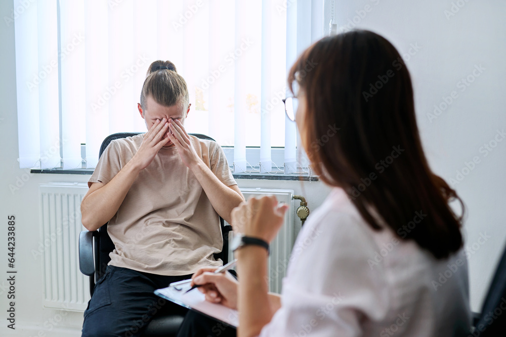 Fototapeta premium Young male student at therapy meeting with college psychologist counselor