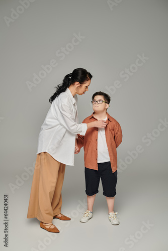 middle aged woman talking to son with down syndrome in eyeglasses on grey, supportive parent