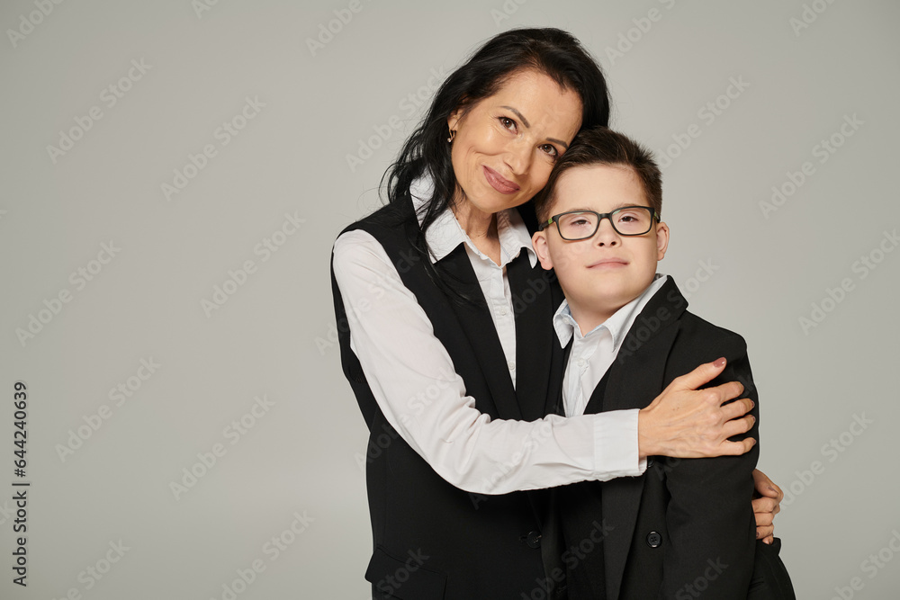 joyful elegant woman embracing son with down syndrome in school uniform on grey, unconditional love joyful elegant woman embracing son with down syndrome in school uniform on grey, unconditional love