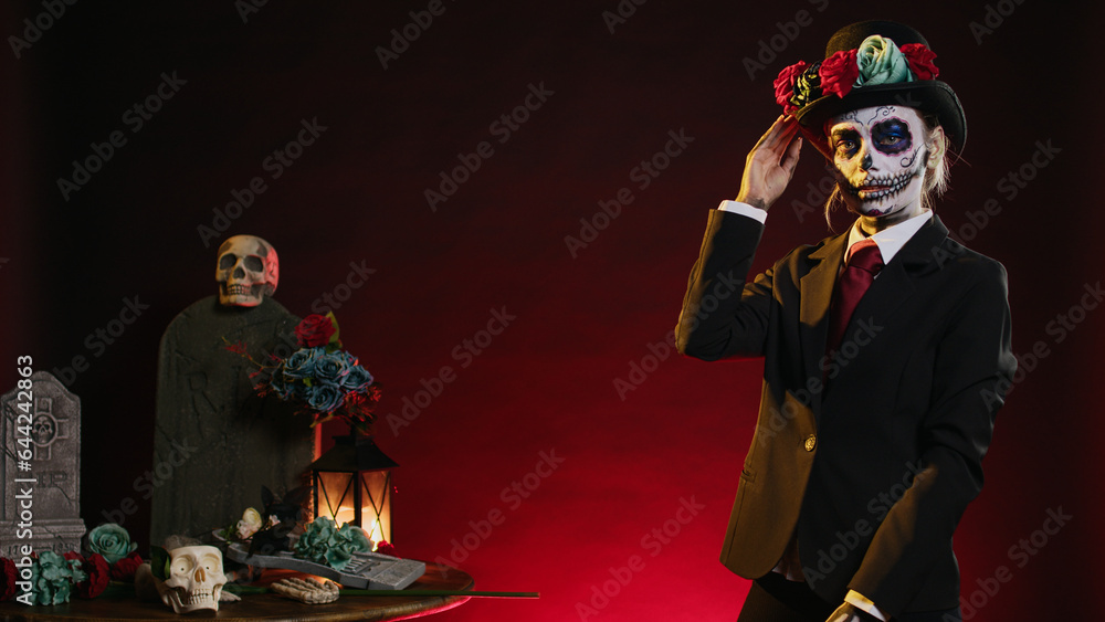 Santa muerte with suit and hat looking mysterious wearing festival skull body art, la cavalera catrina celebrating dios de los muertos in studio. Woman looking like holy mexican entity.
