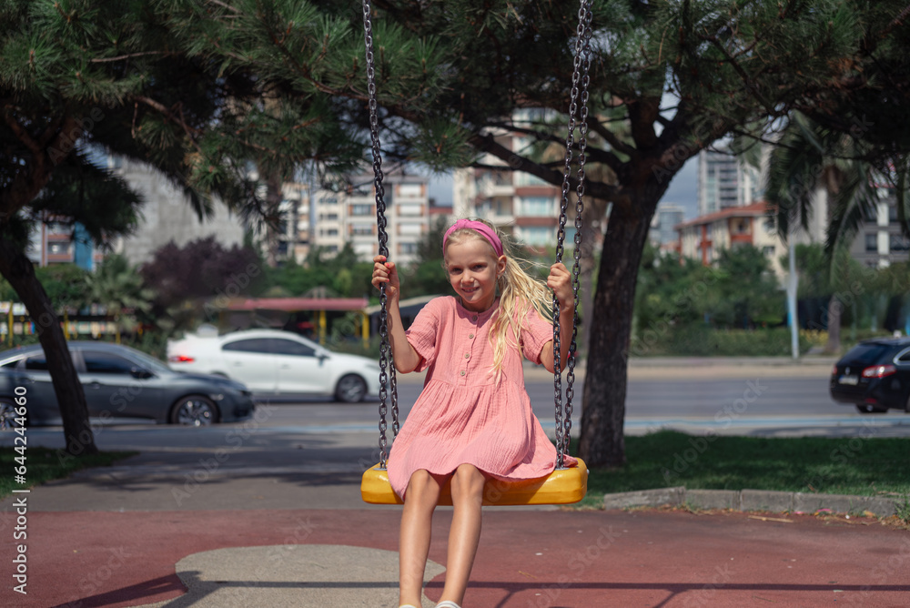 A lively child, dressed in pink, finds pure joy on the swing in the urban park's children's playground. A lively child, dressed in pink, finds pure joy on the swing in the urban park's children's playground.