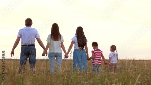 Large family with children raise up joined hands showing happiness at farmland in summer backside view. Daughters and son with parents happy of family holiday. Joyful family with children on meadow