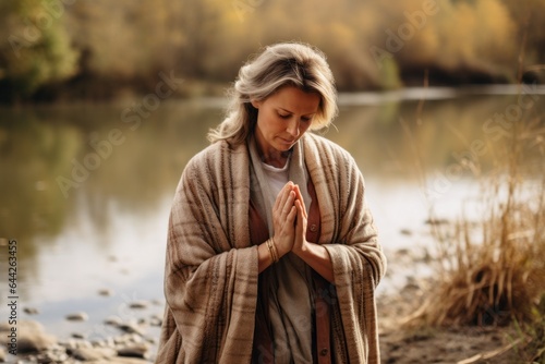 Expressive shot: a standing female aged 50 praying near a river