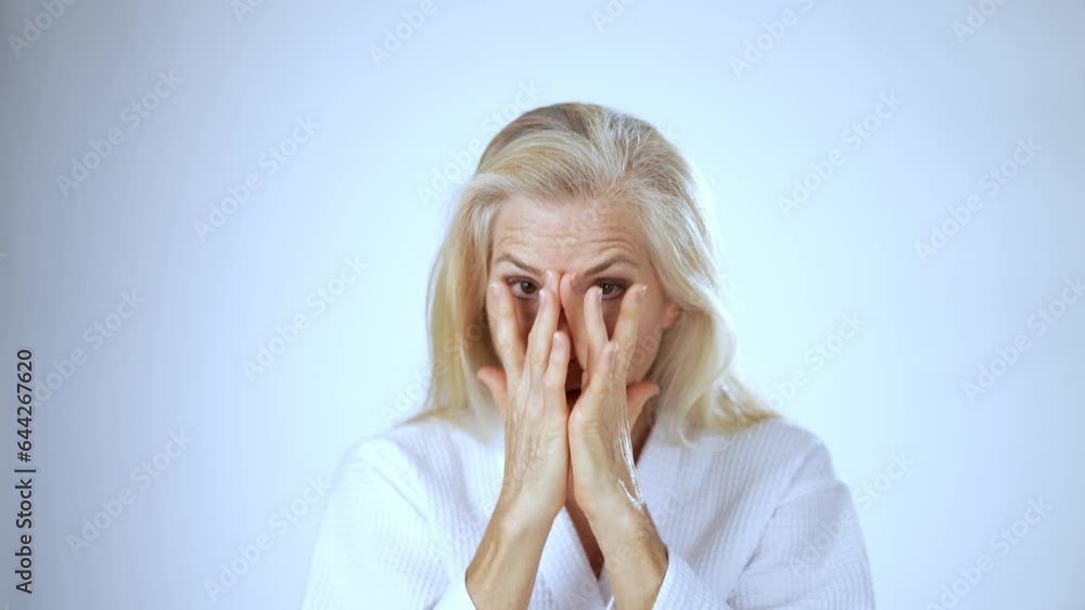 Portrait of middle aged woman wearing robe, massaging her face, applying pampering lotion moisturizer, smiling isolated on studio white background. Portrait of middle aged woman wearing robe, massaging her face, applying pampering lotion moisturizer, smiling isolated on studio white background.