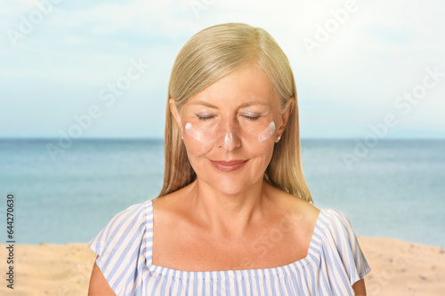 Sun protection. Beautiful young woman with sunblock on her face near sea