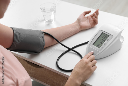 Woman measuring blood pressure with tonometer at table, closeup