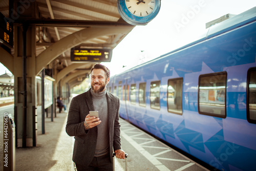 Young man using a smartphone while waiting for his train in a train station photo