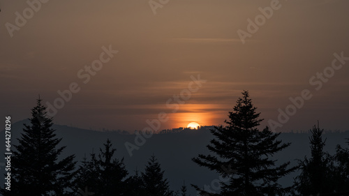 Sunset behind a hill with trees.