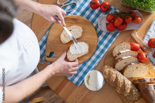 A pregnant young woman spreads curd cheese on slices of bread. View from above