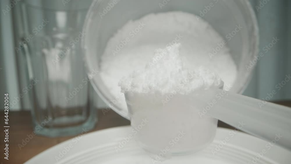 First-person view Using a measuring spoon, I scoop white powder from the jar onto the table. First-person view Using a measuring spoon, I scoop white powder from the jar onto the table.