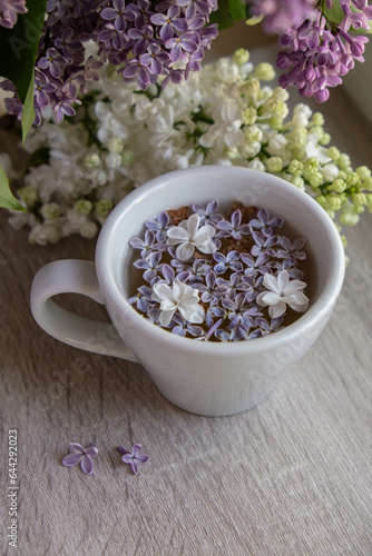 Tasty black tea in white cup on windowsill with aromatic lilac flowers. Spring composition Cup of lilac tea drinking recipe flowering branches of purple lilac. Still life for copy space greeting card