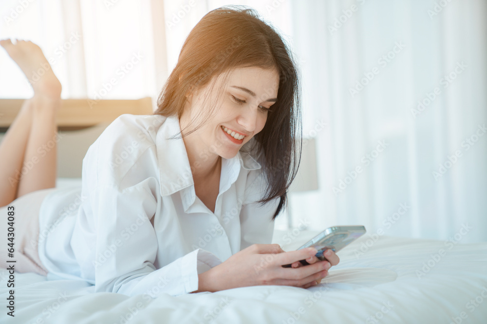 Photo of young happy woman in pajama and holding phone the phone to talk video call Online with friends while sitting on bed. Photo of young happy woman in pajama and holding phone the phone to talk video call Online with friends while sitting on bed.