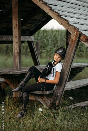 A jockey girl sits on a bench under a canopy, holding a toy horse in her hands.
