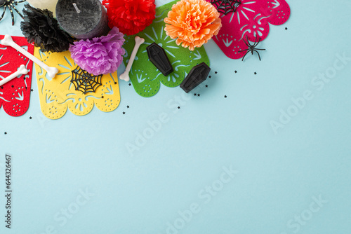 Lively Day of the Dead festivity concept. A top-down photo of a colorful garland amidst vibrant spooky decorations on a light blue isolated backdrop, suitable for text or promotional content