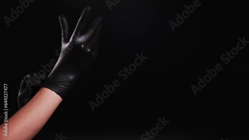 Girl puts on black latex gloves.  Cosmetic services.  Medicine.  Treatments for women. Isolated on black background