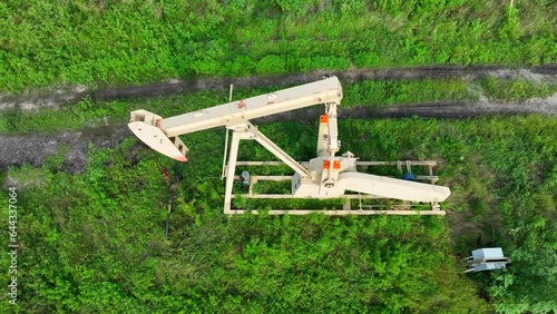 Top down view of oil well drilling and pumping crude oil out of saturated field in USA. Aerial descending shot on pump in action.