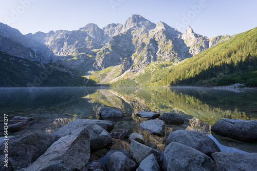 Majestic peak reflecting in pristine crystal clear alpine lake with rocky foreground, Poland, Europe
