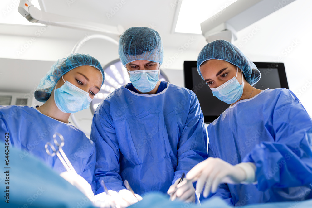 Medical team performing operation. Group of surgeon at work in operating theatre toned in blue. Doctor operation in operation room at hospital concept for insurance advertising. Medical team performing operation. Group of surgeon at work in operating theatre toned in blue. Doctor operation in operation room at hospital concept for insurance advertising.
