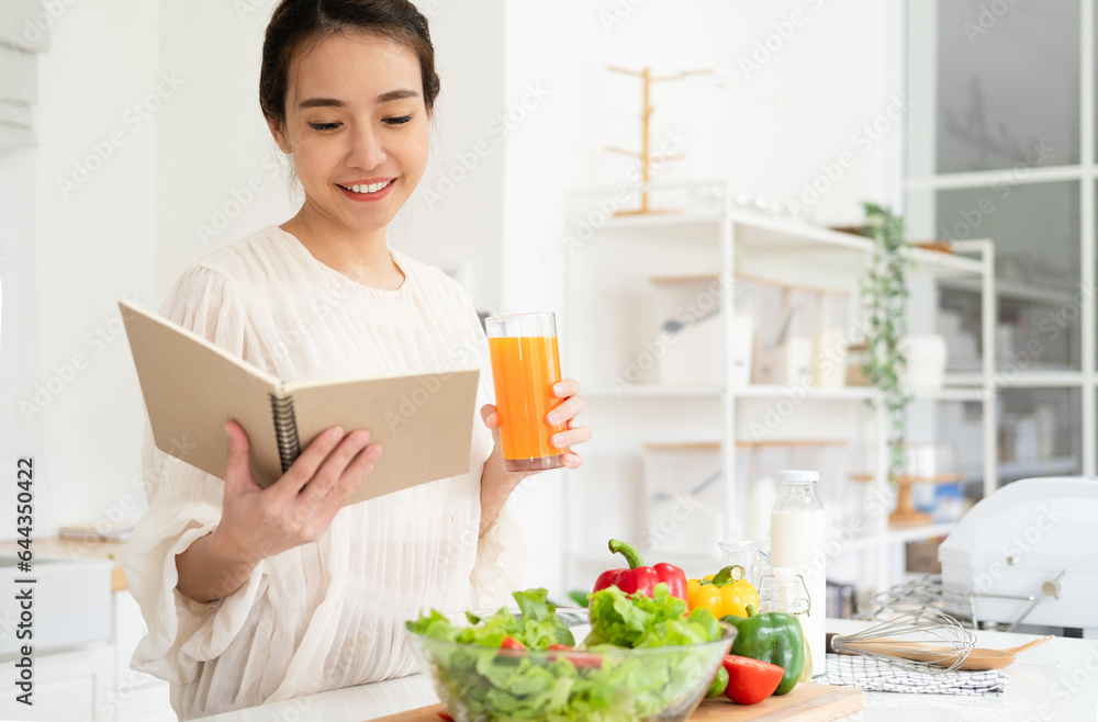 Smiling housewife woman looking at recipe in cookery book preparing vegetable salad cooking food in light kitchen at home. Dieting healthy lifestyle concept. Smiling housewife woman looking at recipe in cookery book preparing vegetable salad cooking food in light kitchen at home. Dieting healthy lifestyle concept.