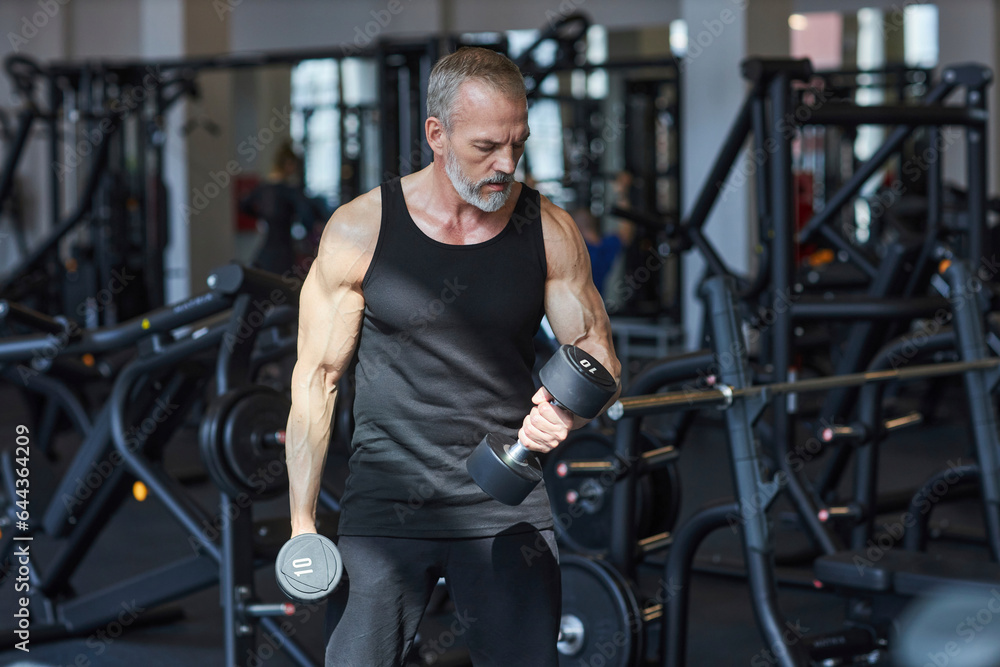 Strong mature man doing exercise with dumbbells in gym
