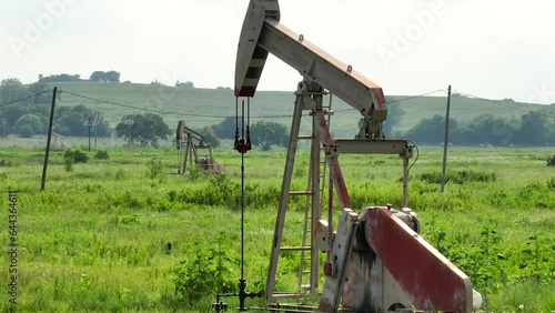 Oil well drilling for crude fossil fuels in rural field in America. United States oil industry theme. Long aerial parallax shot of pump moving.