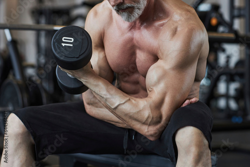 Shirtless man strengthening biceps with barbell in health club