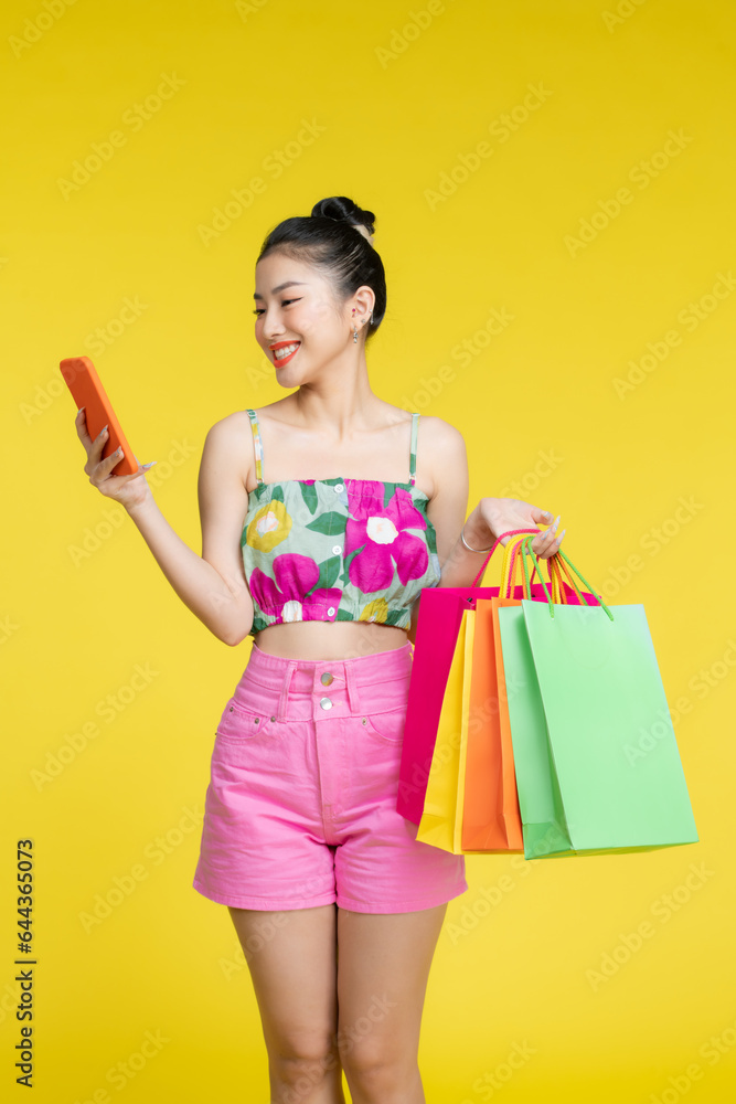 Young energetic Asian woman holding blank use smartphone searching shop retail with colorful shopping bags Young energetic Asian woman holding blank use smartphone searching shop retail with colorful shopping bags