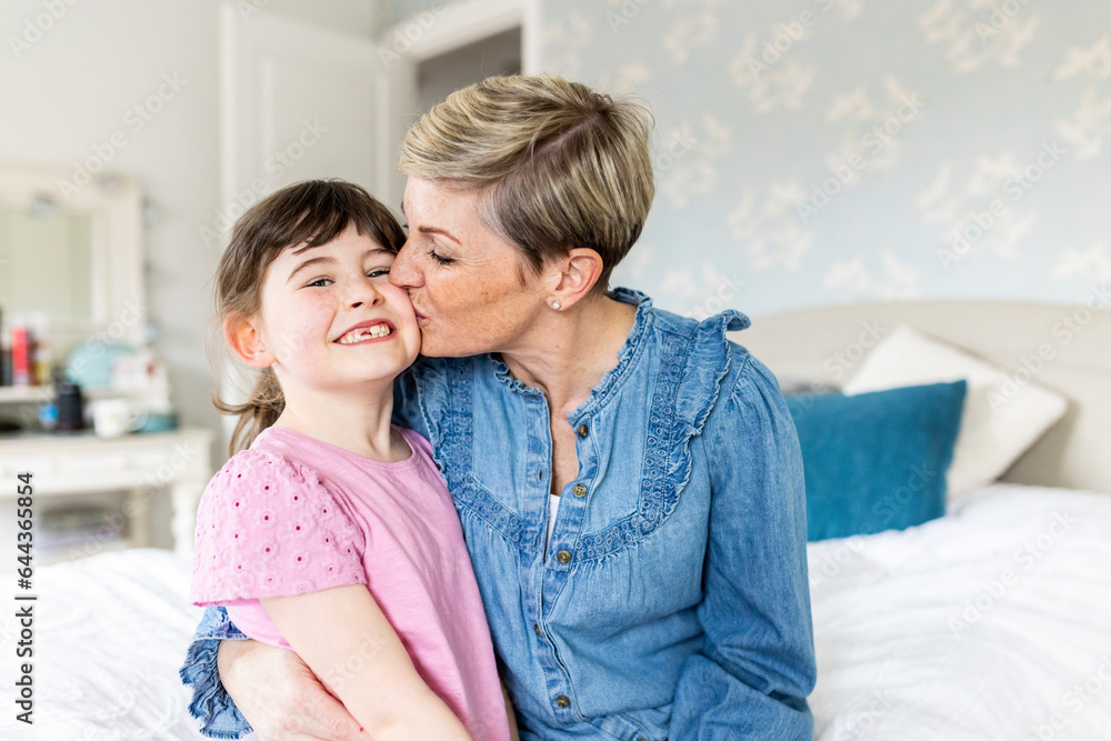 Mother kissing smiling daughter in bedroom Mother kissing smiling daughter in bedroom