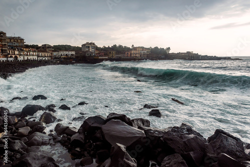 Waves hitting the shore on a cloudy overcast rainy stormy day. Cyclops Coast, black volcanic rocks and send on Sicily, near the town of Acireale photo