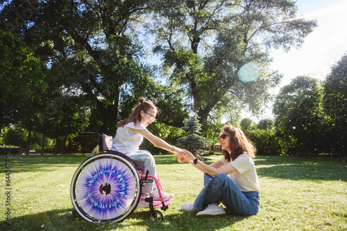 Mother holding hand of daughter sitting in wheelchair on sunny day