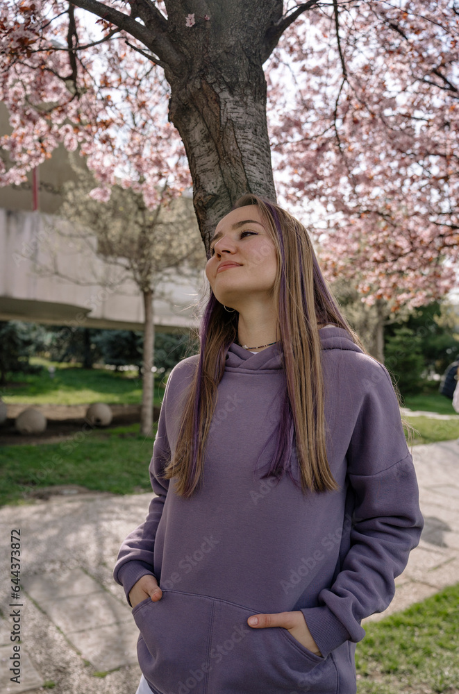 Thoughtful woman with hands in pockets leaning on cherry tree trunk Thoughtful woman with hands in pockets leaning on cherry tree trunk
