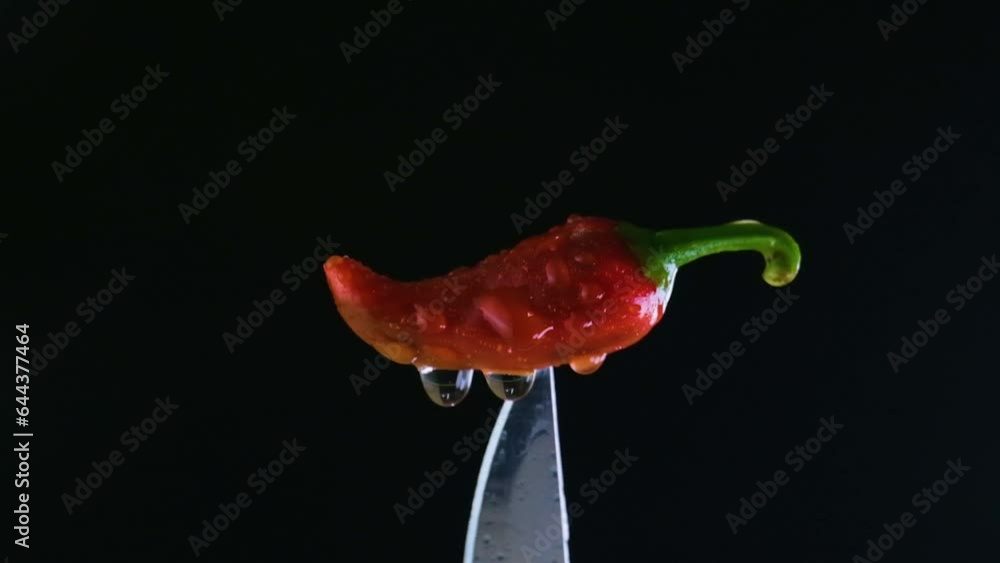 Spicy chili's brilliance, changing light and water drops on red jalapeno above knife