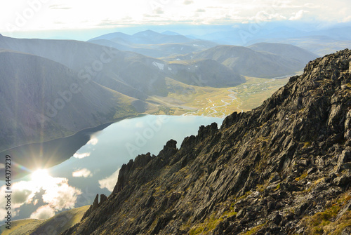 View to the lake high up in the mountains. Reflection of clouds and sun in the lake