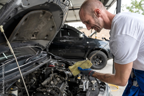Caucasian auto mechanic man checking car engine oil in repair shop