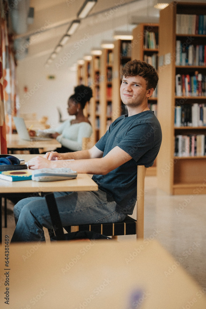Portrait of smiling student sitting at table while studying in library Portrait of smiling student sitting at table while studying in library
